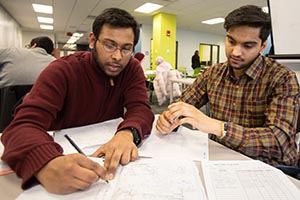 Two seated students looking at notes on the table.